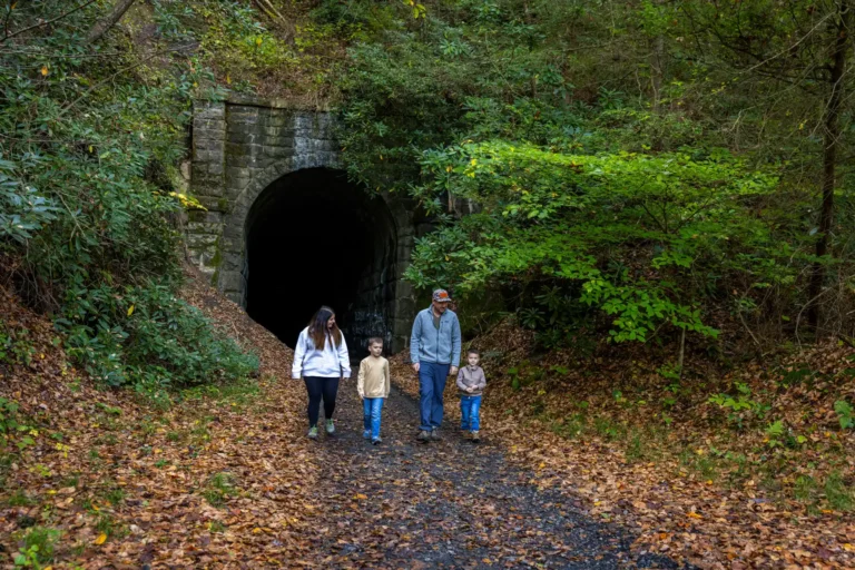family walks out of stone tunnel in forest along gravel rail trail