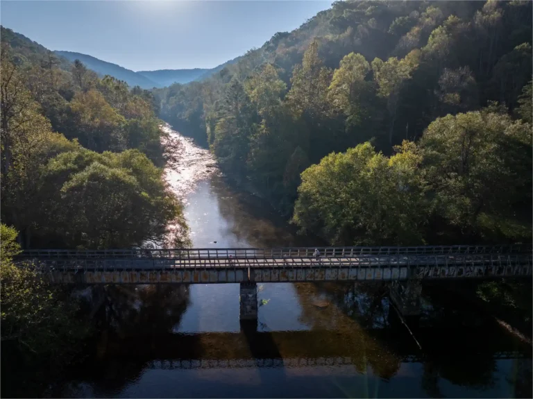 drone photo of river in forested mountains with historic wooden railroad bridge along trail