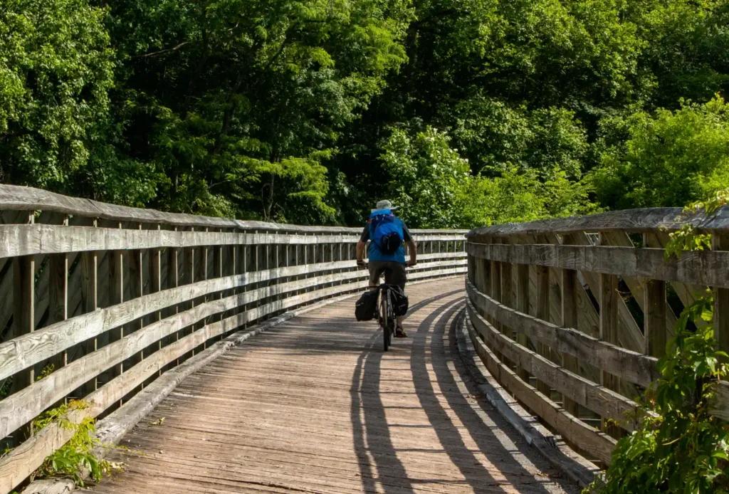 Man on bike rides across wooden rail trail bridge