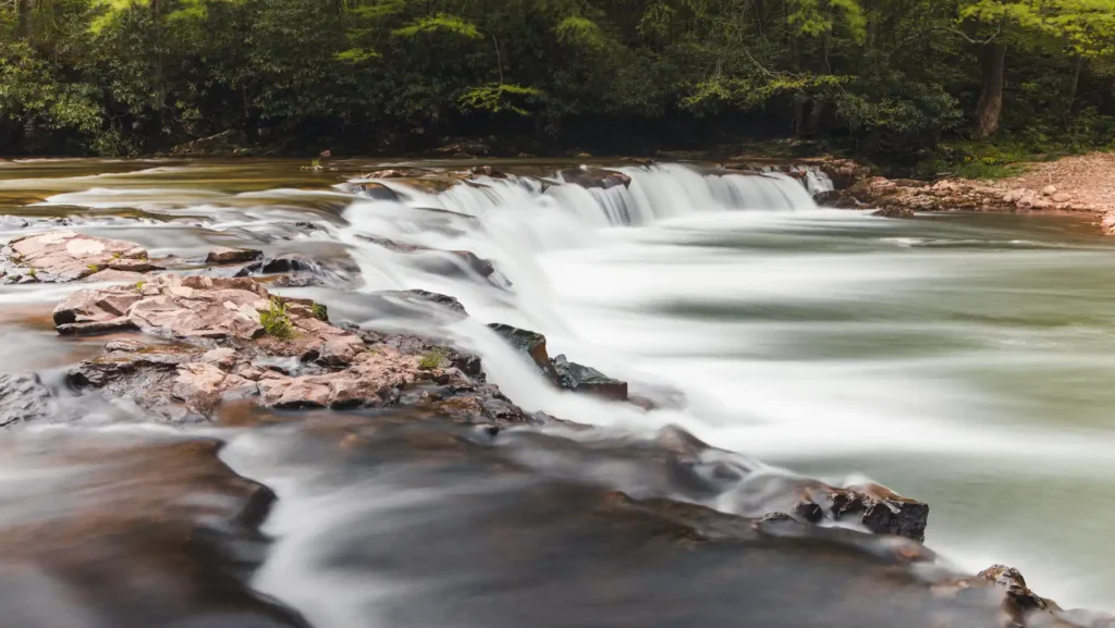Long exposure photograph of wide roadside waterfalls surrounded by trees